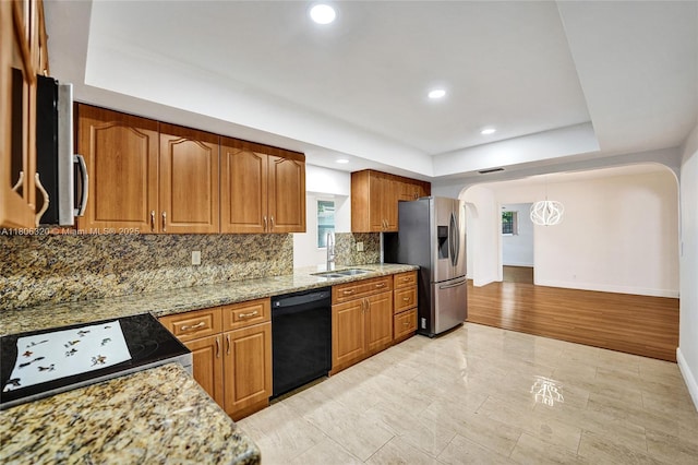 5861 NW 18th Ct, Sunrise, FL 33313 - kitchen featuring appliances with stainless steel finishes, a sink, arched walkways, brown cabinetry, and decorative backsplash