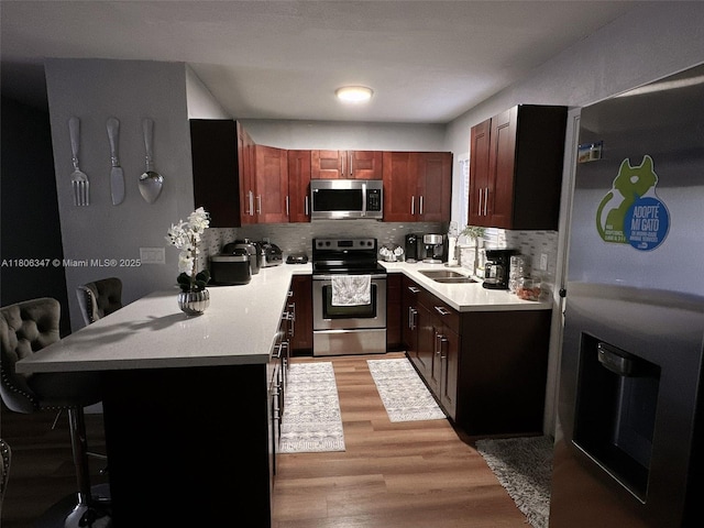 100 NE 171st Ter, Miami, FL 33162 - kitchen with stainless steel appliances, a sink, decorative backsplash, a peninsula, and light wood-style flooring