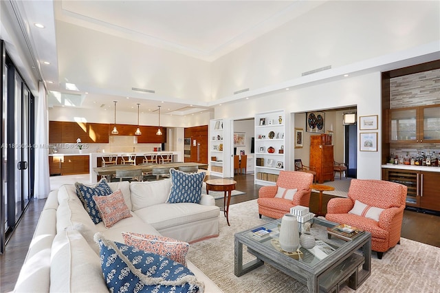 living area featuring a towering ceiling, beverage cooler, a dry bar, wood finished floors, and built in features