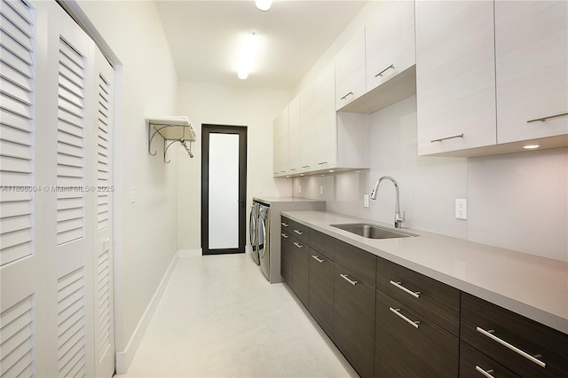 kitchen with a sink, washer and dryer, light countertops, white cabinets, and baseboards