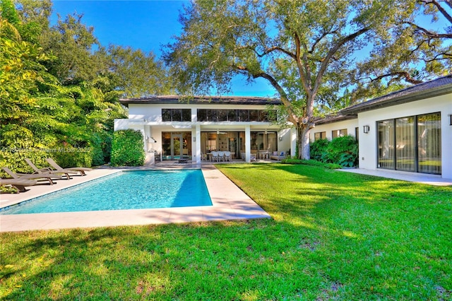 back of house with a patio, a lawn, an outdoor pool, and stucco siding