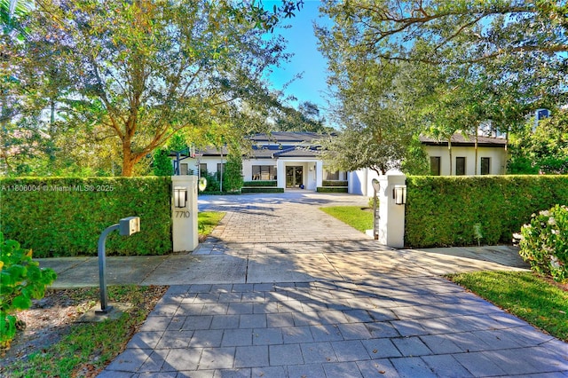 view of property hidden behind natural elements with driveway, a fenced front yard, stucco siding, and a gate