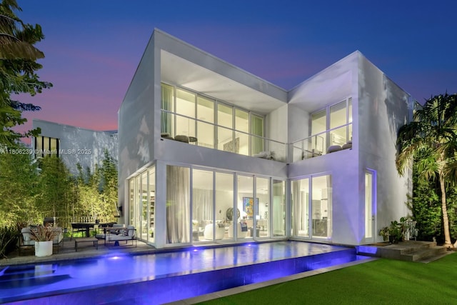 4700 N Meridian Ave, Miami Beach, FL 33140 - back of house at dusk with a balcony, an infinity pool, a patio, stucco siding, and a yard