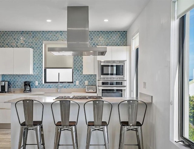 332 Balboa St, Hollywood, FL 33019 - kitchen featuring appliances with stainless steel finishes, island exhaust hood, a sink, white cabinetry, and a kitchen bar