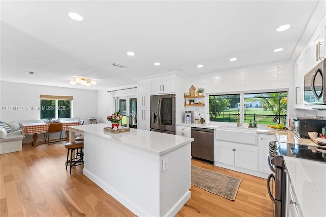 8885 SW 182nd Ter, Palmetto Bay, FL 33157 - kitchen featuring appliances with stainless steel finishes, a center island, white cabinets, light countertops, and a breakfast bar