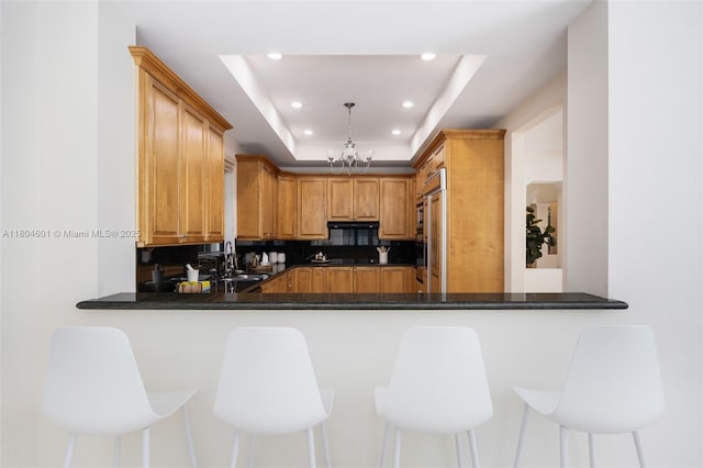 kitchen featuring recessed lighting, dark countertops, a sink, decorative backsplash, and a raised ceiling