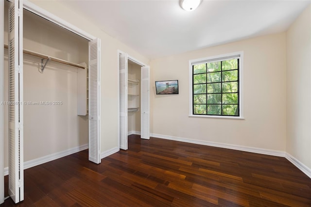 unfurnished bedroom with multiple closets, wood finished floors, and baseboards