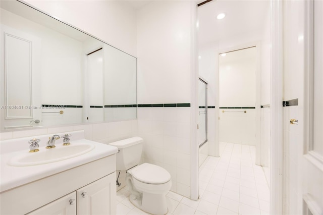 bathroom featuring toilet, vanity, tile patterned floors, a shower, and tile walls