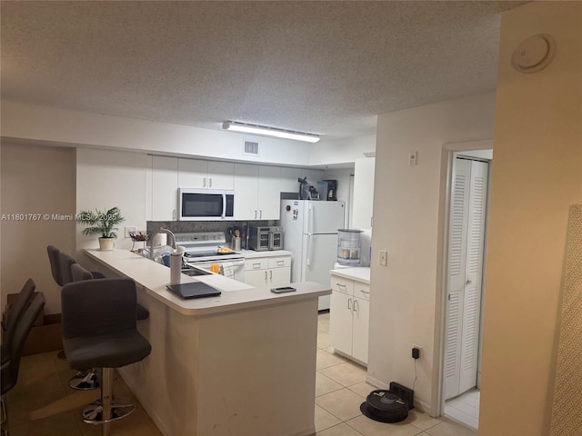 3854 Lyons Rd Unit 207-5, Coconut Creek, FL 33073 - kitchen featuring white appliances, light tile patterned flooring, a peninsula, white cabinets, and a textured ceiling
