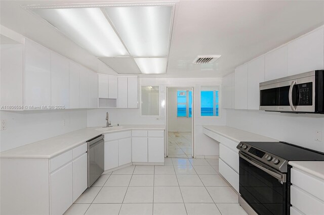 5255 Collins Ave Unit 14D, Miami Beach, FL 33140 - kitchen with appliances with stainless steel finishes, a sink, white cabinetry, and light tile patterned floors