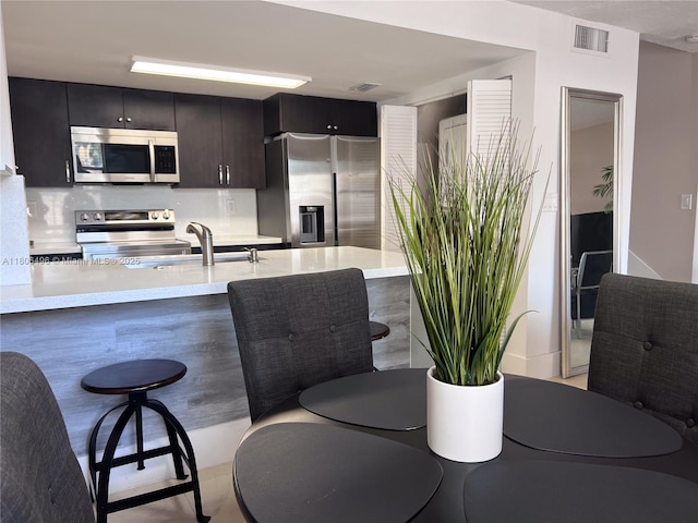 kitchen featuring appliances with stainless steel finishes, a sink, a kitchen breakfast bar, a peninsula, and backsplash