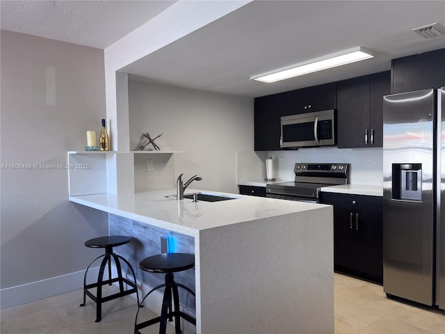 kitchen with appliances with stainless steel finishes, dark cabinets, a sink, and a breakfast bar