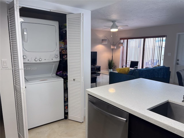 laundry room featuring stacked washing machine and dryer, ceiling fan, a textured ceiling, and light tile patterned floors