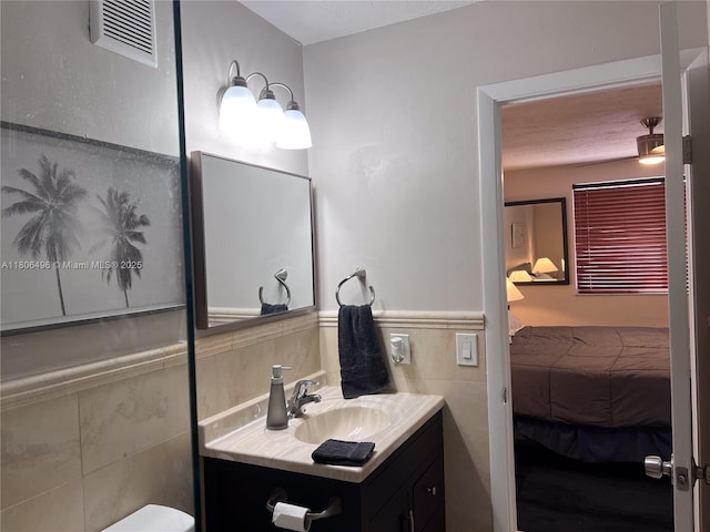 bathroom featuring ensuite bath, vanity, tile walls, and wainscoting