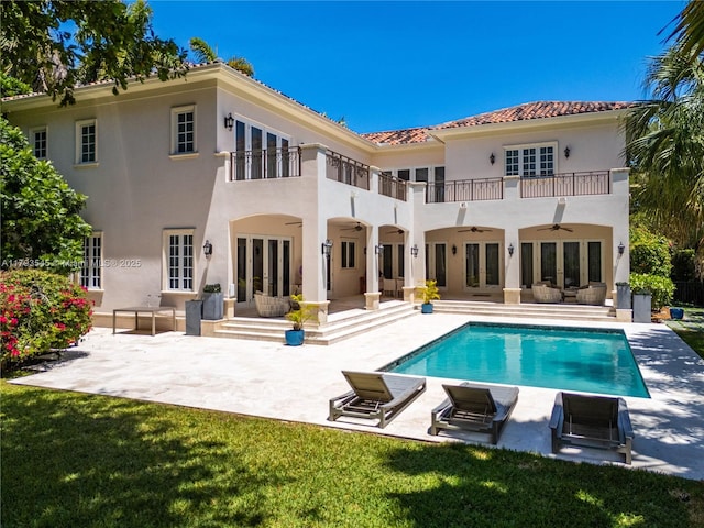 rear view of property with french doors, a ceiling fan, a balcony, stucco siding, and a patio