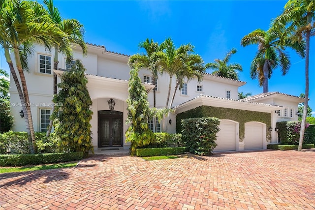 mediterranean / spanish-style house with french doors, stucco siding, a garage, decorative driveway, and a tiled roof