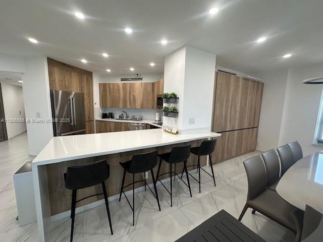 19500 Turnberry Way Unit 12A, Aventura, FL 33180 - kitchen featuring appliances with stainless steel finishes, brown cabinets, a peninsula, recessed lighting, and a kitchen breakfast bar