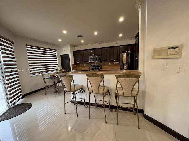 15375 SW 93rd Ln, Miami, FL 33196 - kitchen with appliances with stainless steel finishes, a breakfast bar area, dark brown cabinetry, backsplash, and ornamental molding
