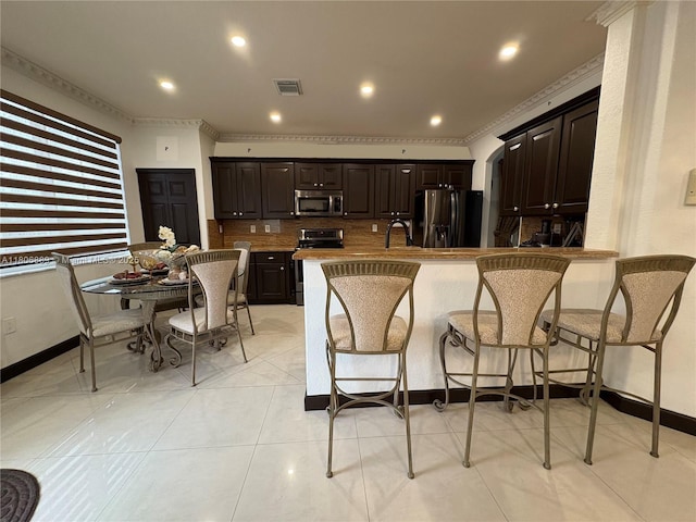 15375 SW 93rd Ln, Miami, FL 33196 - kitchen featuring stainless steel appliances, dark brown cabinetry, a kitchen breakfast bar, crown molding, and a peninsula