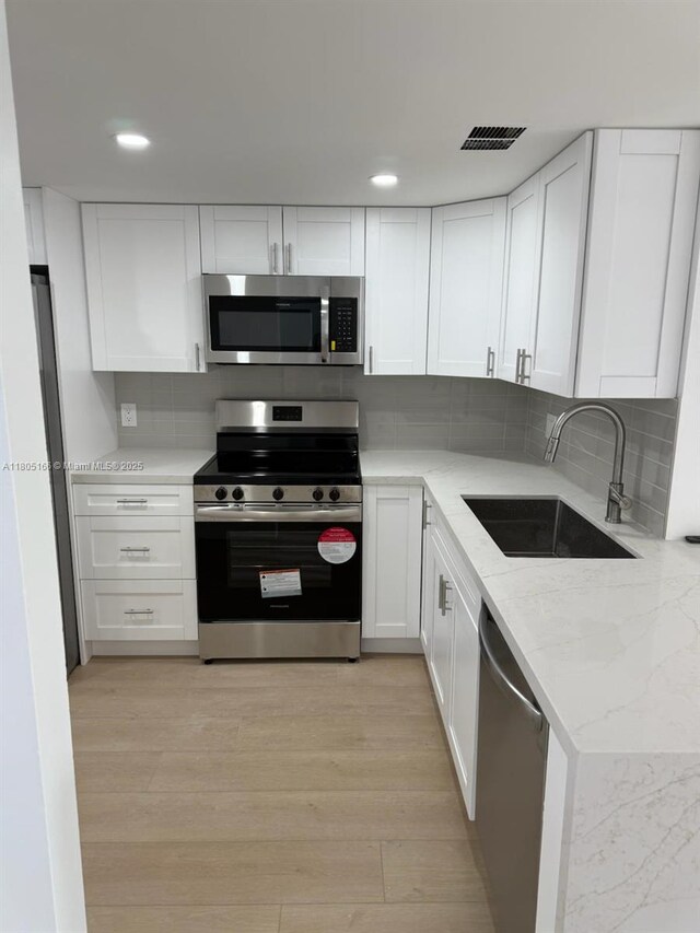 5570 NW 44th St Unit 209A, Lauderhill, FL 33319 - kitchen with stainless steel appliances, white cabinets, light stone countertops, backsplash, and light wood-type flooring