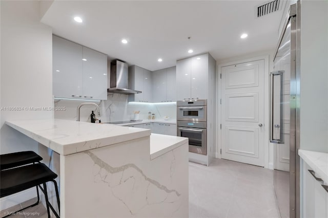 13637 Deering Bay Dr Unit 231, Coral Gables, FL 33158 - kitchen featuring wall chimney range hood, modern cabinets, a peninsula, white cabinetry, and recessed lighting