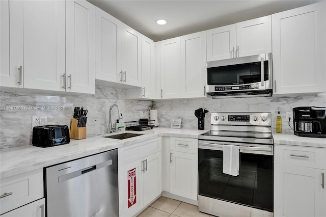 7531 Simms St, Hollywood, FL 33024 - kitchen featuring appliances with stainless steel finishes, a sink, light tile patterned floors, white cabinetry, and backsplash