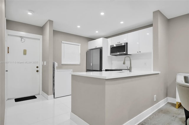 100 Ashbury Rd Unit 103, Hollywood, FL 33024 - kitchen with appliances with stainless steel finishes, washer / dryer, white cabinets, baseboards, and a peninsula
