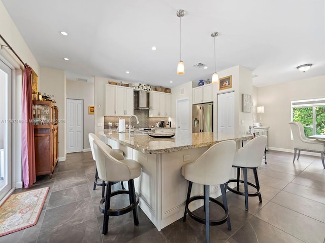 15150 SW 240th St, Homestead, FL 33032 - kitchen featuring stainless steel fridge with ice dispenser, wall chimney exhaust hood, a kitchen bar, tasteful backsplash, and recessed lighting
