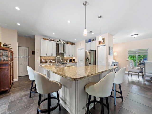 15150 SW 240th St, Homestead, FL 33032 - kitchen with stainless steel refrigerator with ice dispenser, wall chimney range hood, white cabinets, decorative backsplash, and a kitchen breakfast bar