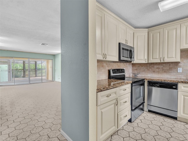 13785 Flora Pl Unit A, Delray Beach, FL 33484 - kitchen featuring stainless steel appliances, backsplash, a textured ceiling, dark stone counters, and cream cabinetry