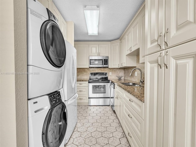 13785 Flora Pl Unit A, Delray Beach, FL 33484 - kitchen with appliances with stainless steel finishes, stacked washer / drying machine, cream cabinetry, a textured ceiling, and dark stone countertops