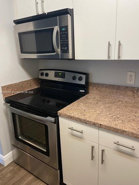 927 Riverside Dr Unit 326, Coral Springs, FL 33071 - kitchen featuring appliances with stainless steel finishes, wood finished floors, white cabinetry, baseboards, and light stone counters