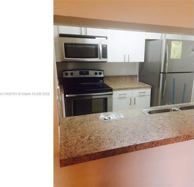 927 Riverside Dr Unit 326, Coral Springs, FL 33071 - kitchen featuring appliances with stainless steel finishes, white cabinets, light stone countertops, and a sink