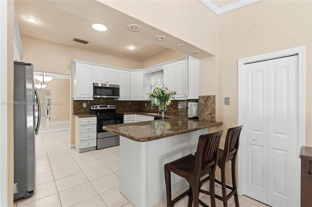 1090 Meadowlark Ave, Miami Springs, FL 33166 - kitchen featuring stainless steel appliances, a peninsula, white cabinetry, decorative backsplash, and dark stone counters