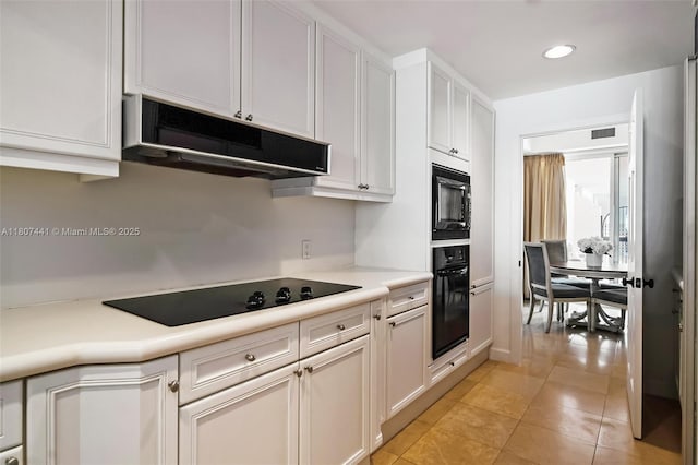 5235 Fisher Island Dr Unit 5235, Miami Beach, FL 33109 - kitchen featuring black appliances, under cabinet range hood, light countertops, white cabinetry, and light tile patterned flooring