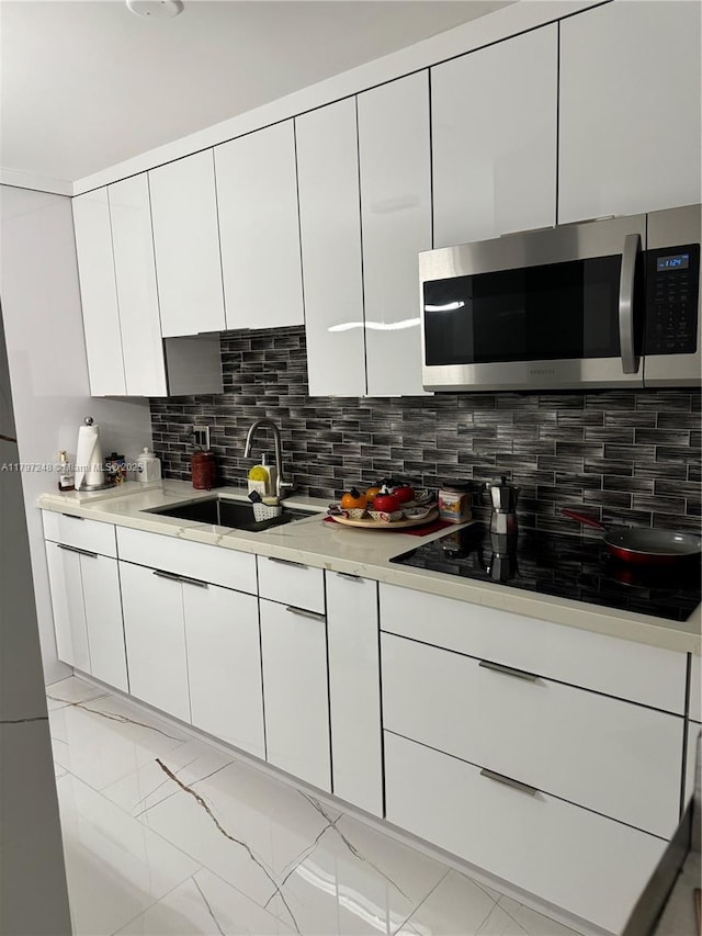 6055 W 19th Ave Unit 216, Hialeah, FL 33012 - kitchen with stainless steel microwave, a sink, black electric stovetop, white cabinets, and tasteful backsplash