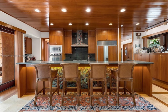 5725 N Bayshore Dr, Miami, FL 33137 - kitchen featuring built in appliances, wall chimney exhaust hood, wood ceiling, brown cabinetry, and tasteful backsplash