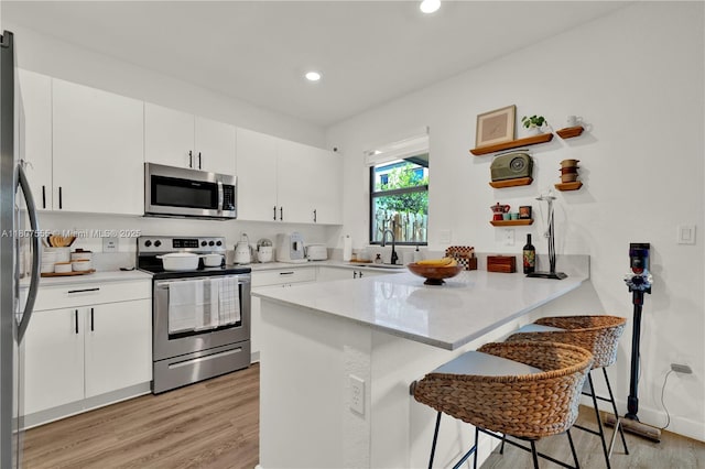 12982 SW 232nd Ln, Miami, FL 33170 - kitchen featuring stainless steel appliances, a peninsula, light wood-style floors, a breakfast bar area, and white cabinets