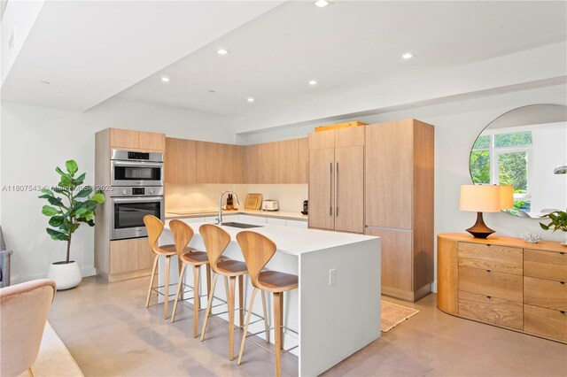 455 NE 39th St Unit 102, Miami, FL 33137 - kitchen featuring double oven, concrete flooring, modern cabinets, a kitchen breakfast bar, and light countertops