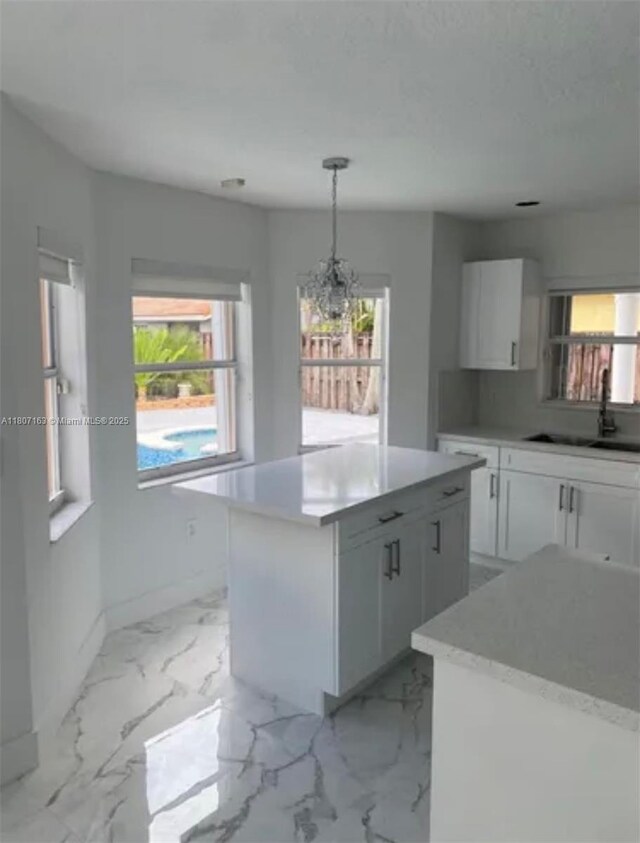 16461 SW 100th Ter, Miami, FL 33196 - kitchen featuring a sink, a kitchen island, white cabinets, decorative light fixtures, and light marble finish floors
