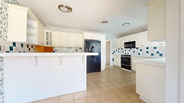17535 SW 91st Ave, Palmetto Bay, FL 33157 - kitchen with black appliances, a peninsula, decorative backsplash, a kitchen bar, and light tile patterned floors