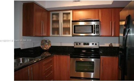 3232 SW 22nd Ter Unit 1003, Miami, FL 33145 - kitchen with appliances with stainless steel finishes, brown cabinets, a sink, glass insert cabinets, and dark stone counters