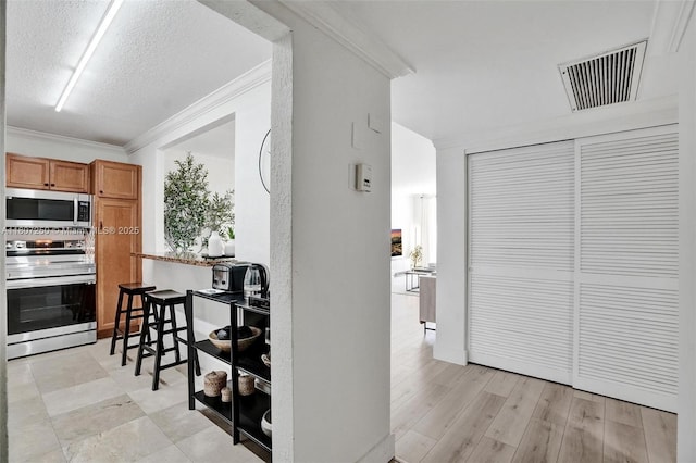 19380 Collins Ave Unit 718, Sunny Isles Beach, FL 33160 - kitchen featuring appliances with stainless steel finishes, crown molding, a kitchen bar, a textured ceiling, and brown cabinets