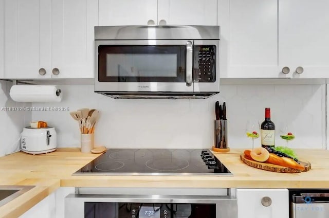 7326 Collins Ave Unit 201, Miami Beach, FL 33141 - kitchen view of stainless steel microwave, white cabinetry, light countertops, and black electric cooktop