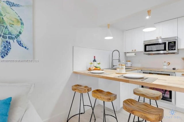 7326 Collins Ave Unit 201, Miami Beach, FL 33141 - kitchen featuring stainless steel microwave, a sink, a breakfast bar, white cabinetry, and wood counters