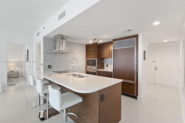 495 Brickell Ave Unit 2304, Miami, FL 33131 - kitchen featuring wall chimney range hood, built in appliances, a sink, light tile patterned floors, and a breakfast bar