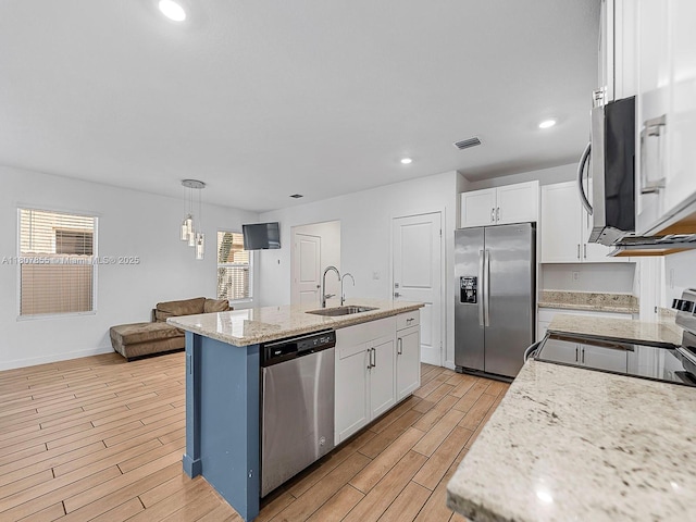 501 NE 6th Ct, Florida City, FL 33034 - kitchen featuring stainless steel appliances, a sink, white cabinets, light wood finished floors, and a center island with sink