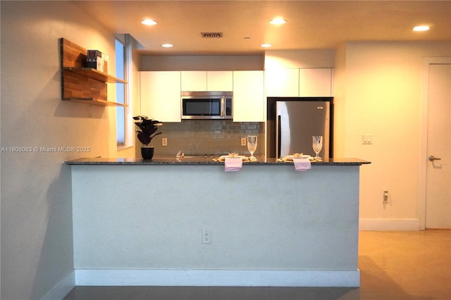 1050 Brickell Ave Unit 202, Miami, FL 33131 - kitchen with stainless steel appliances, white cabinetry, a peninsula, baseboards, and decorative backsplash