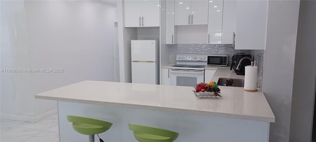 650 E 55th St, Hialeah, FL 33013 - kitchen with white appliances, white cabinetry, light marble finish flooring, a peninsula, and decorative backsplash
