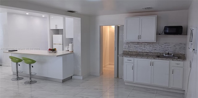 650 E 55th St, Hialeah, FL 33013 - kitchen featuring black microwave, light marble finish floors, freestanding refrigerator, backsplash, and a breakfast bar